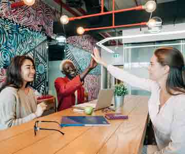 Three women smiling and high-fiving to celebrate business success.