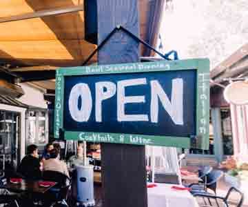 Wooden framed sign hanging on outdoor posts, displaying “Open.”