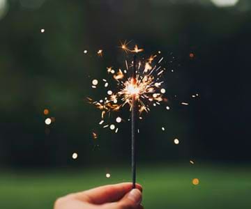 The tip of a sparkler that is lit in front of a dark background.