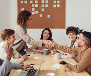 A group of co-workers sitting around a table. Two of the co-workers are shaking hands.