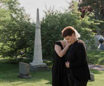 Two women wearing all black and grieving in a grave yard.