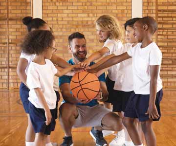 Young Kids Sports Team In Basketball Court Smiling And Putting Their Hands On Basketball With Coach