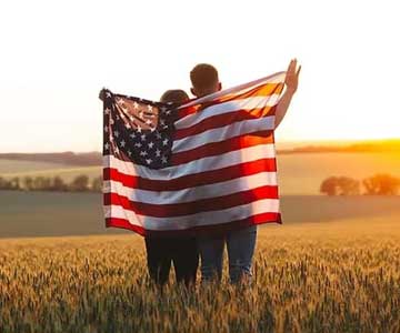 Happy Couple Holding Up United States Flag Near Sunset.