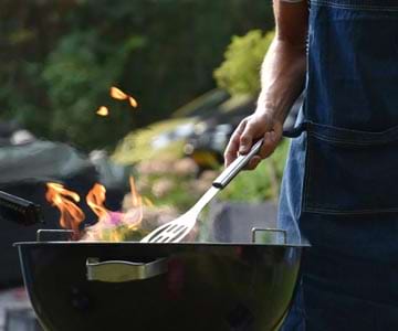A close up of a person holding a spatula to a grill with a flame.