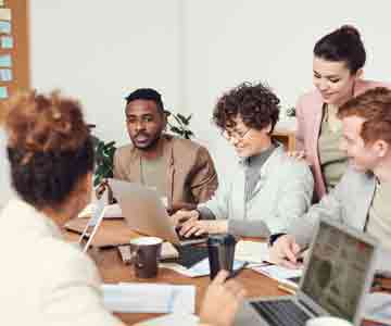 People happily working together on a long desk with laptops.