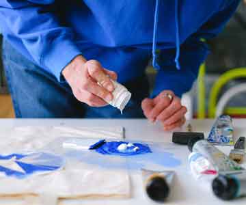 Woman mixing white and blue paint on a desk for stencil work.