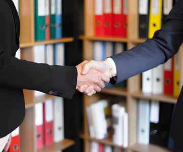 Two people shaking hands, wearing suits.