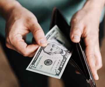 Person’s hands holding a wallet, pulling out a five-dollar bill. 