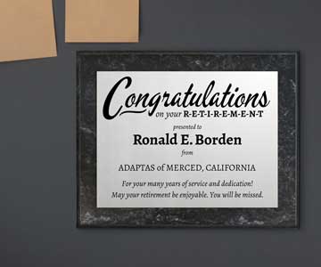 Silver metal retirement plaque on a marble board, proudly displayed on a desk.