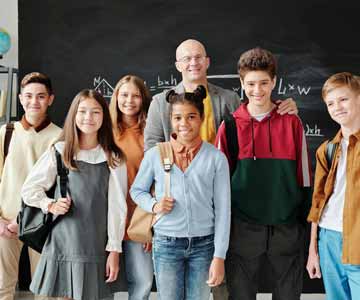 Group Of Young Students In Class With Teacher In Front Of Blackboard Smiling For Picture