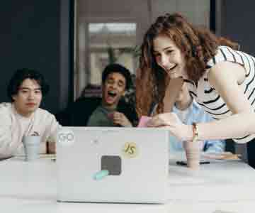 3 employees gathered, smiling at a laptop screen.