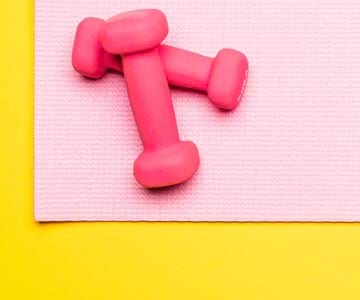 Pink dumb bells on a pink yoga mat on yellow flooring