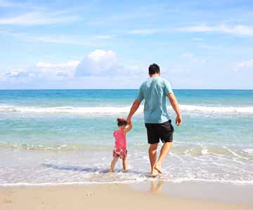 A father holding his daughter's hand, walking along the beach.