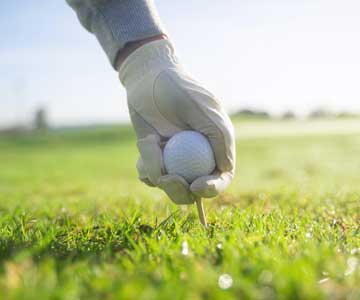 A hand placing a golf ball and a tee in the green.