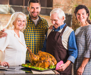 Happy Family Holding Each Other Inside Kitchen Standing Around An Island Countertop With A Cooked Turkey Roast
