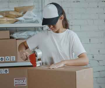 Woman in warehouse taping a box shut.