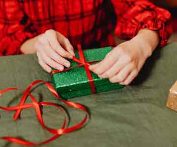 Person in red checkered sweater wrapping a Christmas gift.