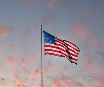 The American flag blowing in the wind with a sunset behind.