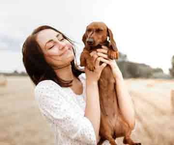 Woman smiling with a sleek brown Dachshund.
