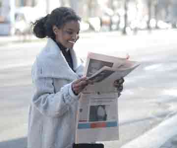 Woman wearing a laboratory coat, reading a newspaper.