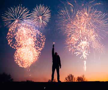 Man holding sparkler with fireworks on the background