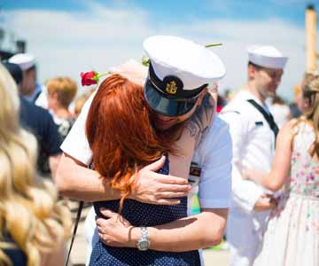 A Navy sailor hugging a red haired woman.