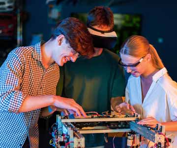 Three Pairs Of Hands Working On Technology Project Featuring Metal Parts And Colored Wiring