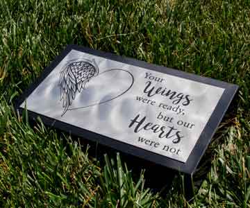 Small granite headstone with a titanium plate, resting quietly on a bed of green grass.