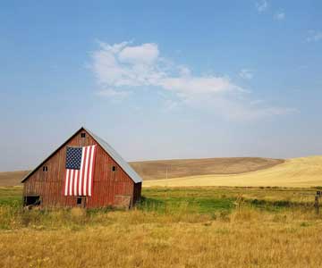 A rustic barn with an American Flag hanging on the front.
