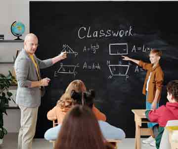 A teacher pointing to a lesson on a blackboard with student next to them.
