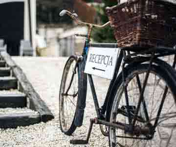 An old bicycle with a wicker basket and a frame sign that reads “RECEPCJA.”