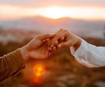 Two hands holding each other with beautiful sunset in the background.