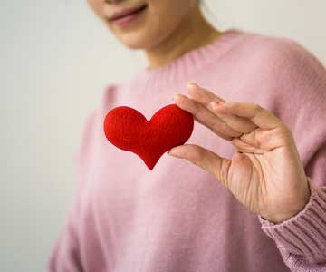 A woman in a pink sweater, holding a toy heart.