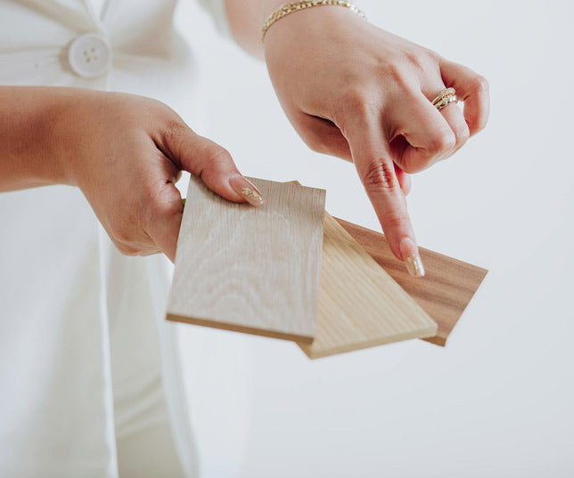 Woman Hands Holding Three Small Samples Of Different Wood Types And Pointing To The Darkest Wood Sample