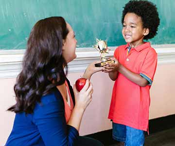 A little boy student gives his teacher a small star-shaped trophy award. 