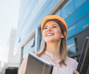 Woman in a hard hat, holding plans and smiling.