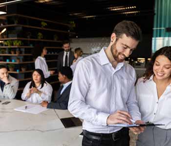 Two colleagues looking over something in an office full of people.