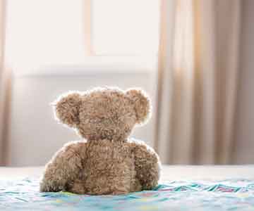 Teddy bear sitting on the bed, facing away.
