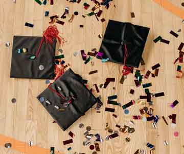 Three graduation caps laying on a gym floor, surrounded by confetti.