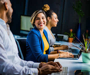 Three Coworkers In Business Clothes Laughing Together And Using Computers At A Long Work Desk In Office