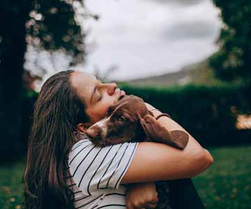 A calm woman hugging her beloved dog outside.