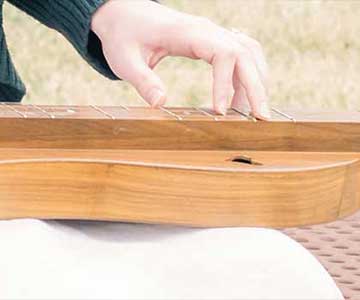 A Young Woman Playing A Mountain Dulcimer At The Park