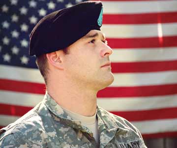 A veteran standing at attention with an American flag in the background.