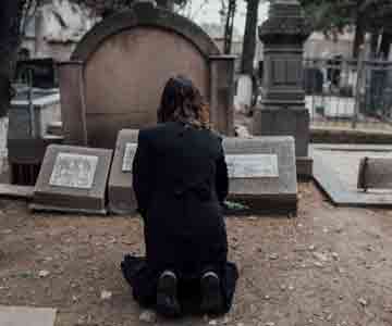 Woman kneels quietly before a grave, lost in remembrance.