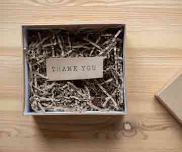 An open gift box with a thank you card on wood table.