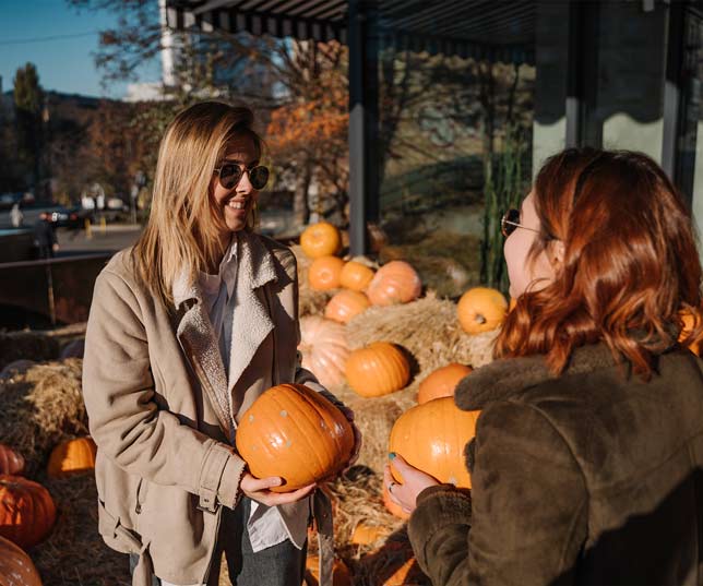 Happy Woman With Sunglasses Buying A Pumpkin From Small Business Pumpkin Patch Outdoors Near Stacks Of Hay