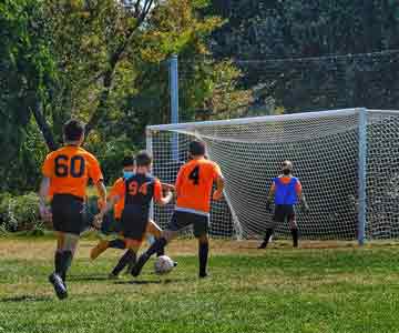 Young boys playing soccer, kicking the ball towards the other teams goal.