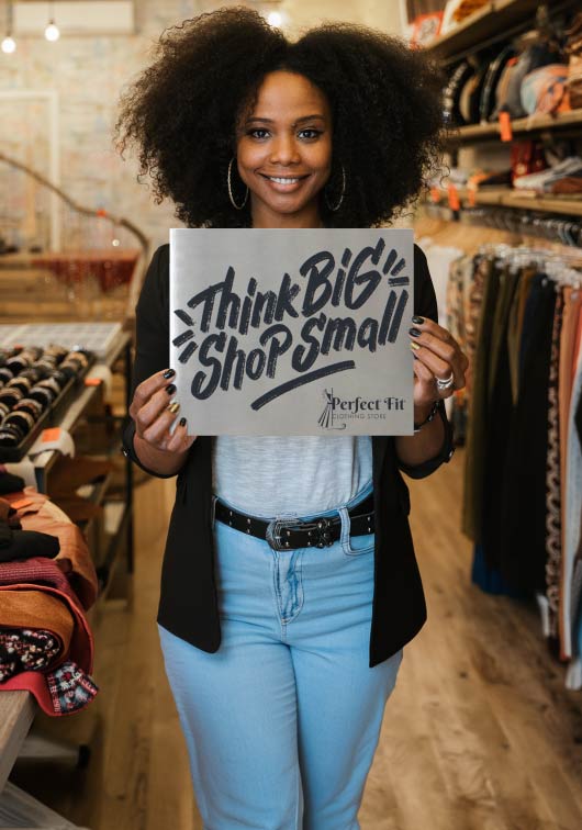 A woman holding a custom stainless steel sign that says 'Think Big Shop Small' in a store setting.