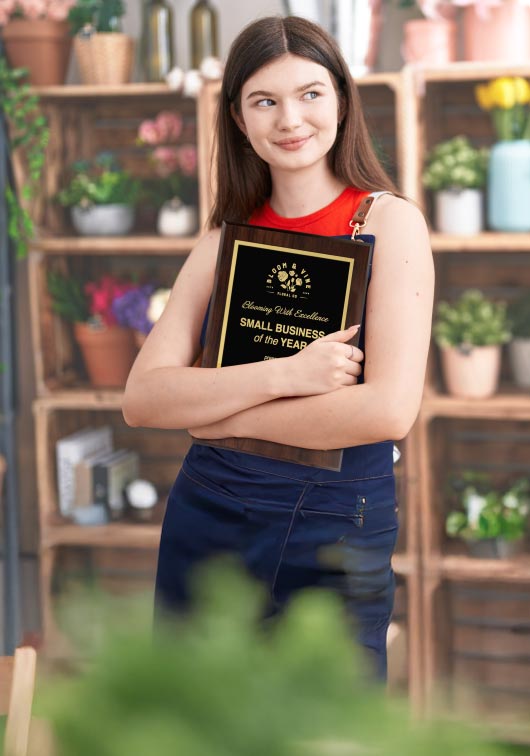 Florist Holding A Laser Engraved Aluminum Plaque For Small Business Of The Year In Front Of Plants.