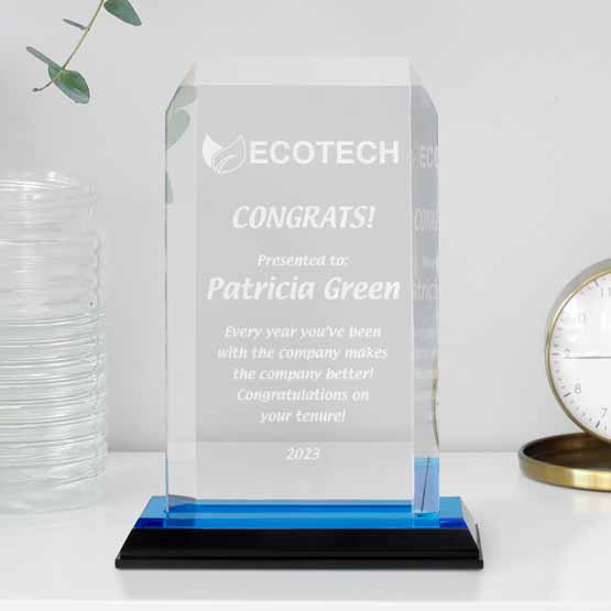 Custom Acrylic Award With Clipped Corners Featuring Logo And Name And Message And Blue Mirror Base On White Shelf With Clock